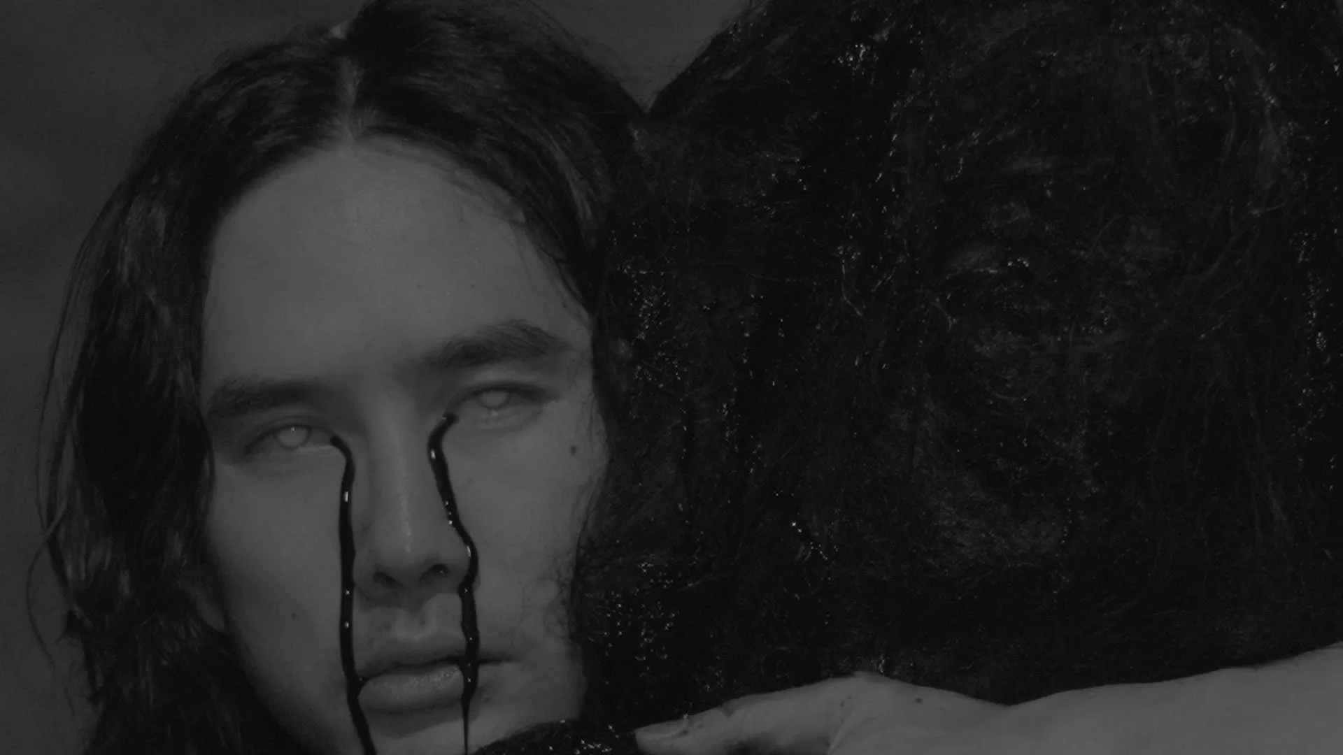 An asian person with long wavy hair crys black liquid while embracing another person with black liquid running throught their long black hair. 