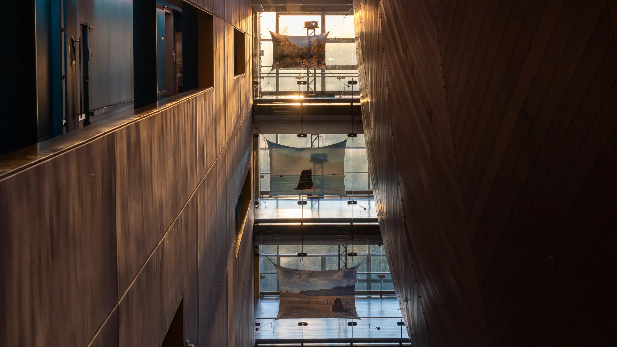 three pieces of material with projections on them across three levels of a building with glass walls of light shining through