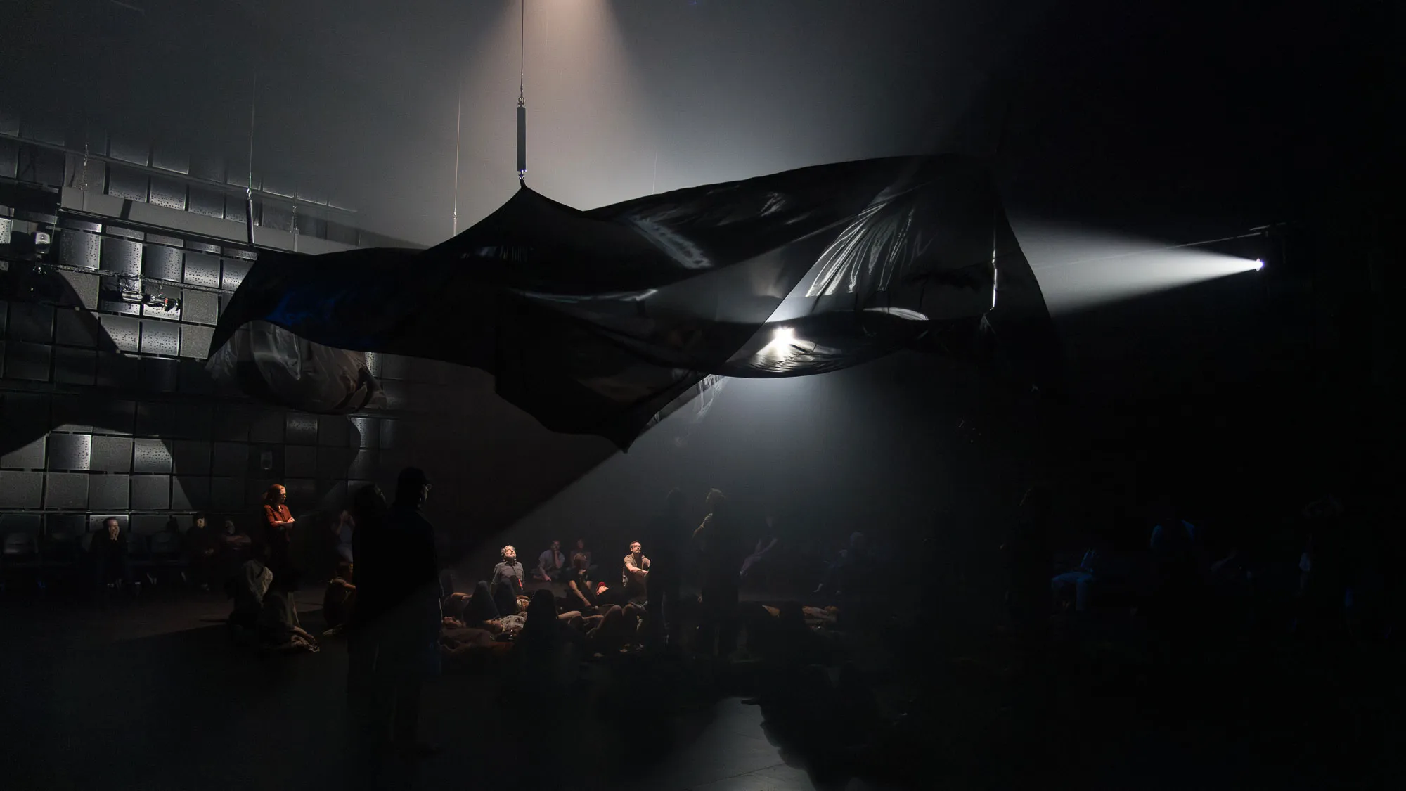 an ominous black canvas of fabric undulates above an audience in a black box studio