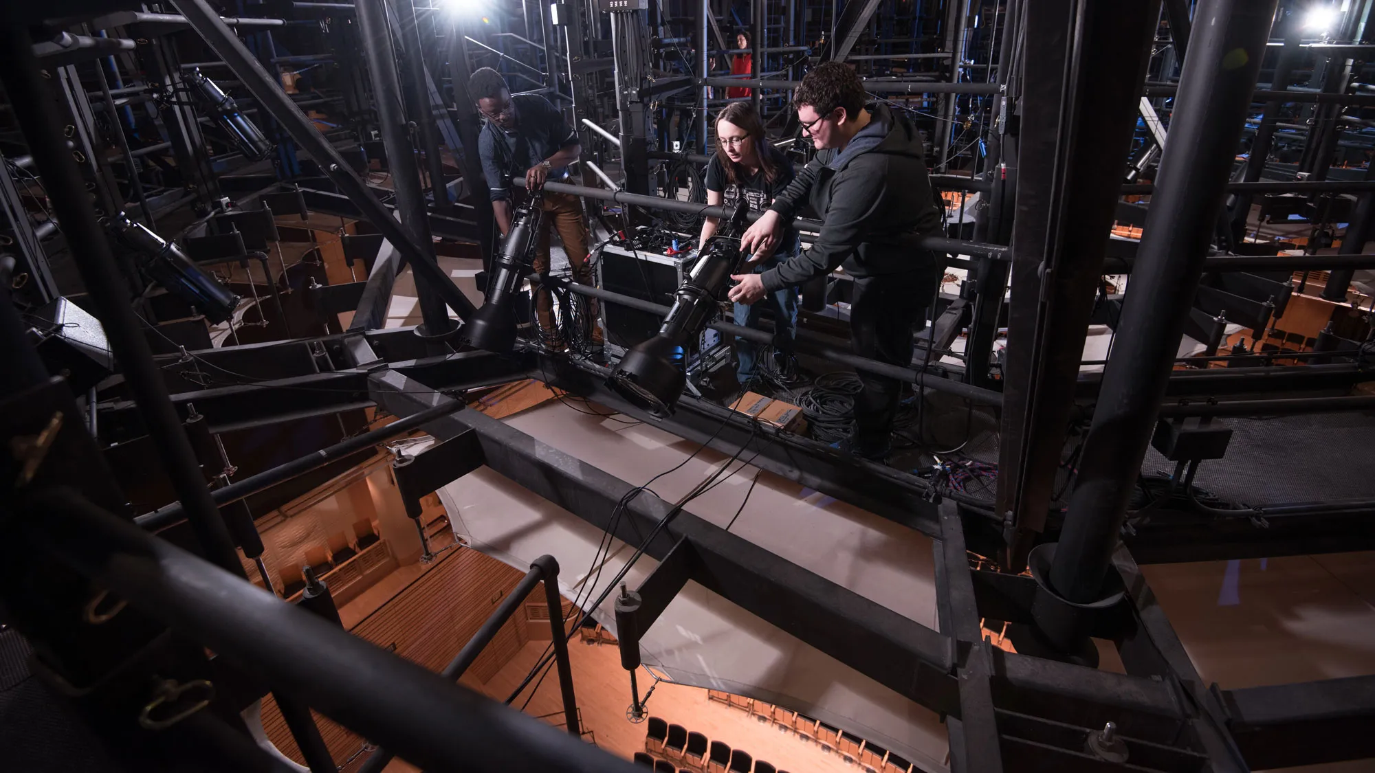 two people adjusting some lights in a grid above a studio