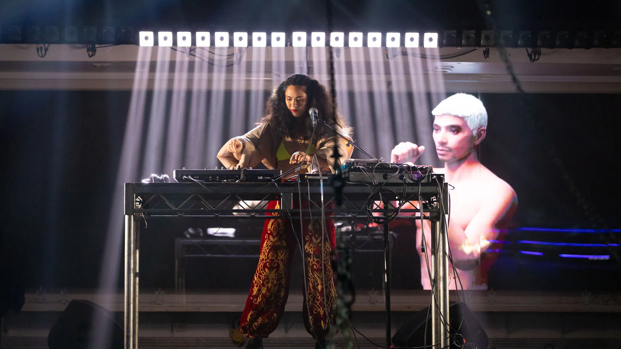 a woman at a keyboard with an image projection of a shirtless man in the background