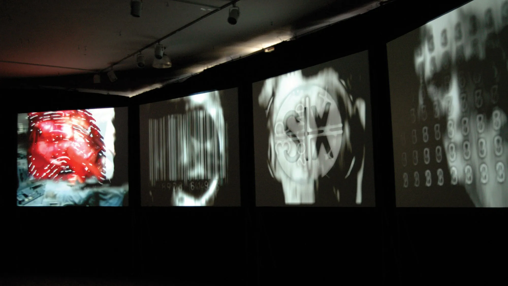 Four large screens on a dark background projecting three abstract black and white images and one of an up close bloody fingerprint. 