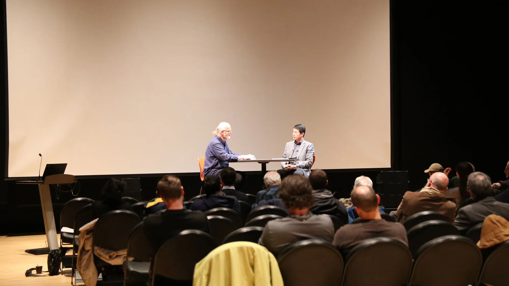 Johannes Goebel and Hui Su in discussion in front of a seated crowd. 