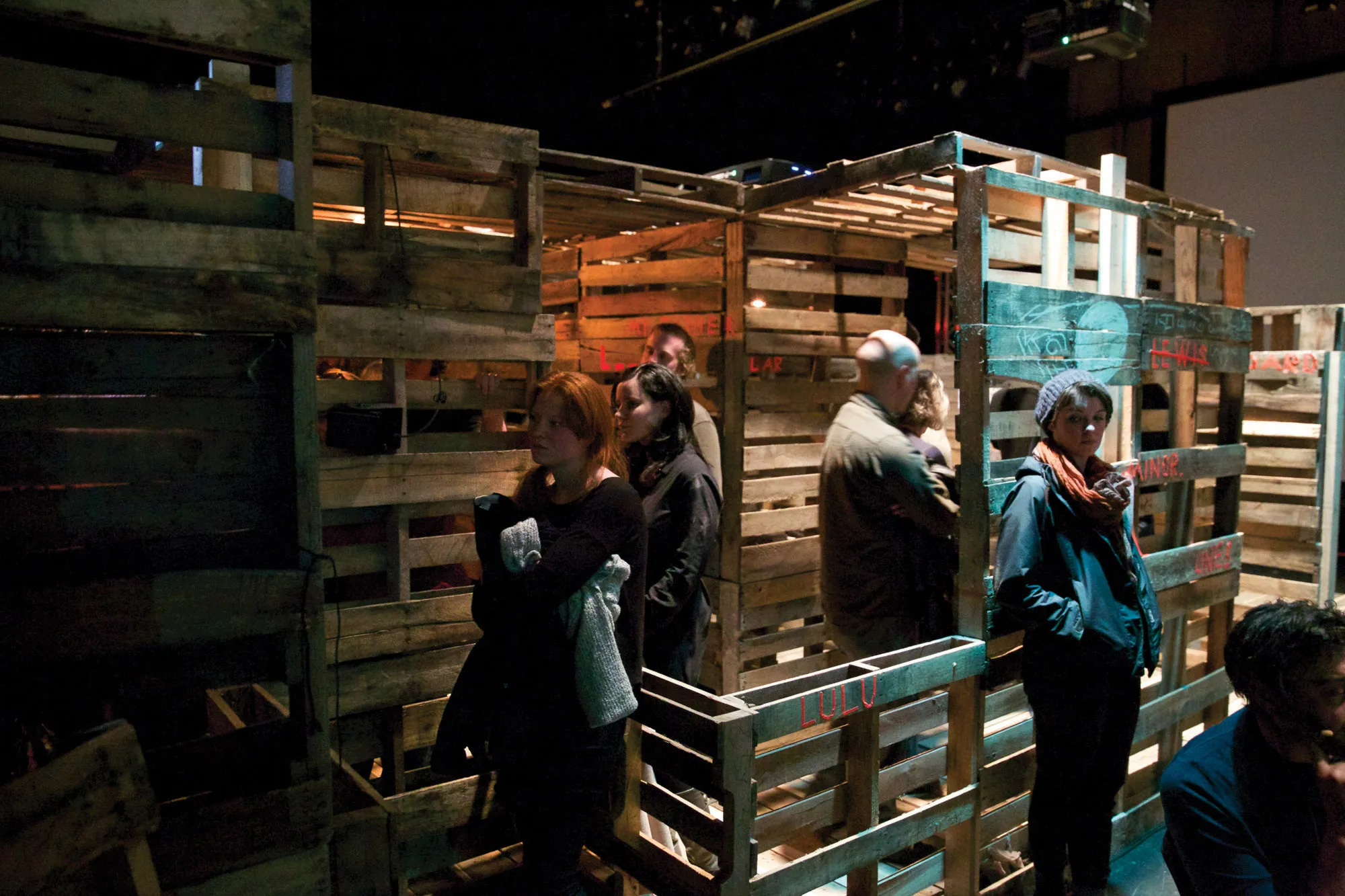 People walking though and contemplating a maze of wooden palettes 