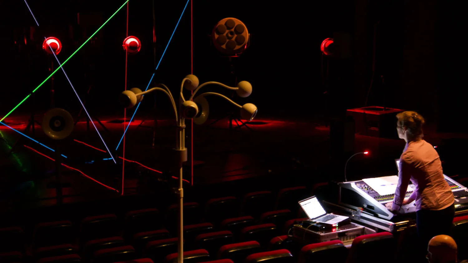 A woman at an audio mixer with abstract yellow objects and blue, red, green, and purple lines being projected in 3D into the stage in front of her. 