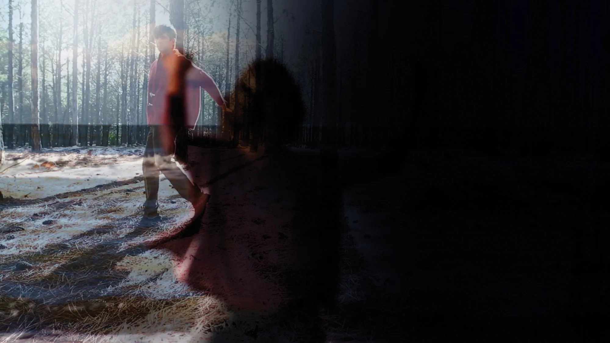 A double exposed image of a shadow of a woman reaching and a man wearing a red jacket walking through a sun dappled forest. 