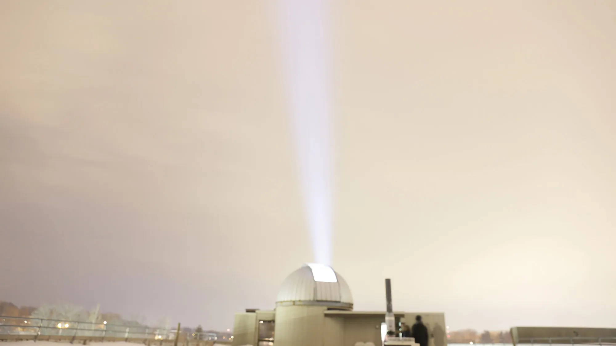 An observatory shooting a beam of light into a gray hazy sky. 